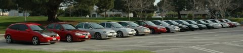 1991 Ford Taurus - A line of sedans and a red hatchback are parked in a lot on a sunny day.
