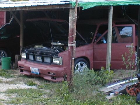 1998 Ford Taurus - A red pickup truck sits under a makeshift shelter with its hood open, revealing the engine bay.