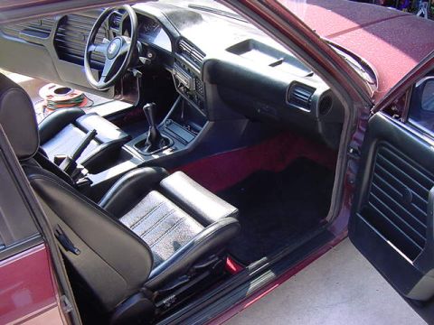 1984 BMW 3 Series - The interior of a maroon 1984 BMW 3 Series shows black leather seats and a manual transmission shifter.