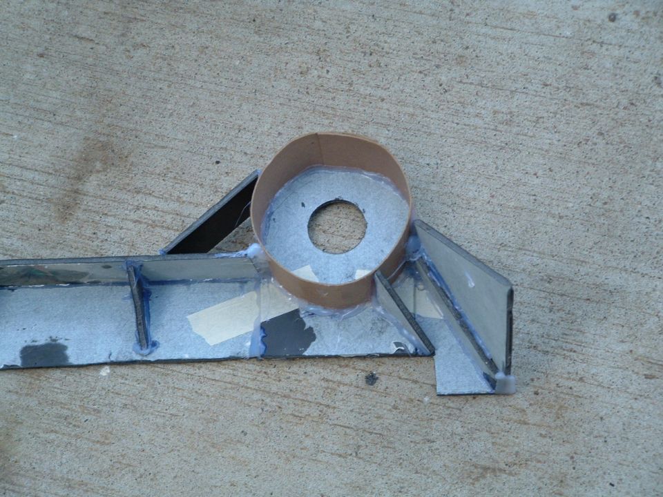 Close-up of welded sheet-metal bracket with a tube collar and tape mockup on concrete