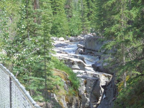 1988 Ford Bronco - A scenic view of a river flowing through rocks, surrounded by dense forest and a partial view of a fence.