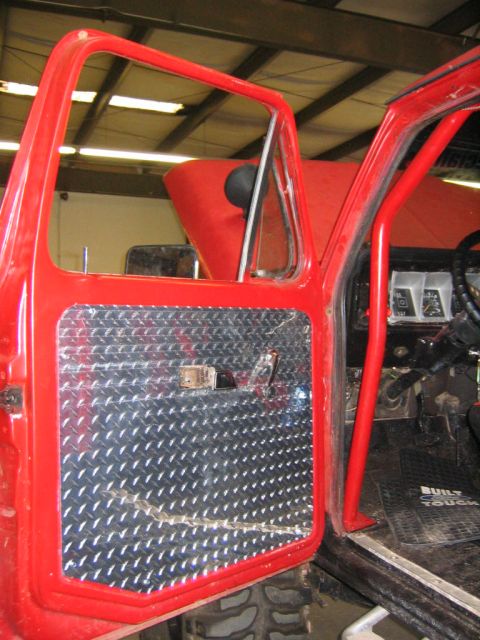 1979 Ford Bronco - Open red truck door showing a diamond-plate aluminum door panel replacing the stock trim, with the interior beyond revealing a red roll cag…