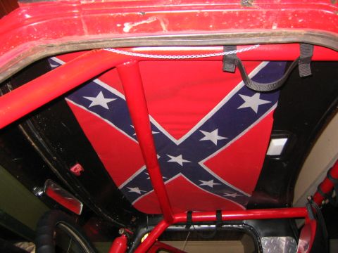 1979 Ford Bronco - The interior of a vehicle is visible, a red roll cage and a confederate flag as a headliner.