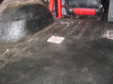 1979 Ford Bronco - The interior of a vehicle shows a black textured floor and a red seat with a roll bar in the background.