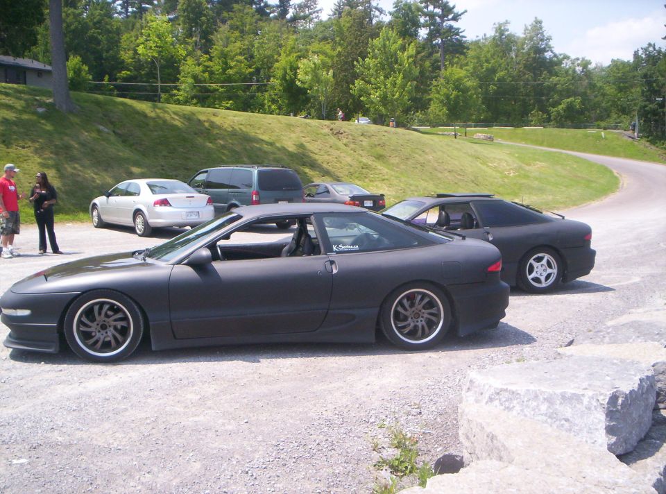 Matte black lowered coupe on gravel lot with second black coupe behind