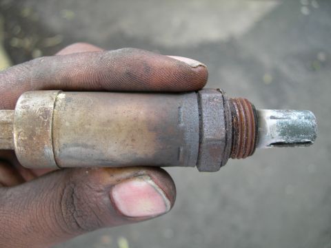 1992 Ford Taurus - A dirty, used oxygen sensor is held in a hand, showing its metal construction and threaded attachment point.