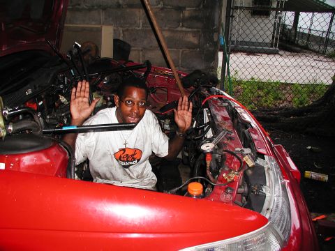 1992 Ford Taurus - Mechanic working on the engine of a red car, with hands raised.