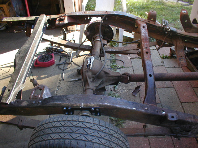 rusted vehicle frame, rear axle, and tire on brick paving