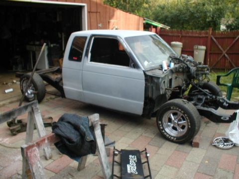 1998 Ford Taurus - A light gray pickup truck chassis with its cab is parked outside a garage, undergoing some work.
