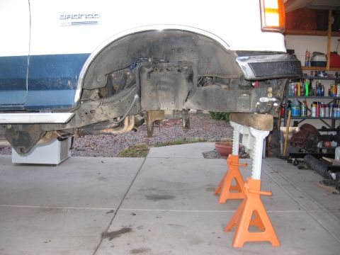 1990 Ford Bronco - The rear section of a 1990 Ford Bronco is elevated on jack stands for maintenance, revealing its undercarriage.