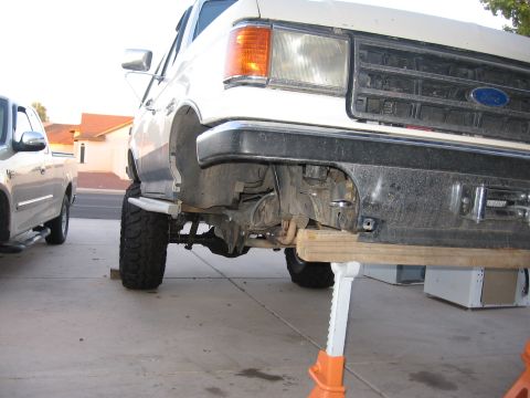 1990 Ford Bronco - Front view of a white 1990 Ford Bronco showing its lifted suspension and custom bumper, supported by jack stands.
