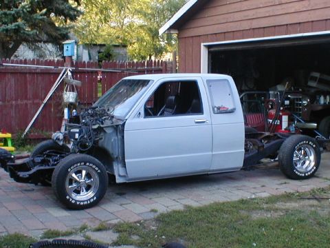 1998 Ford Taurus - A white pickup truck chassis is parked outside a garage with its front end disassembled.
