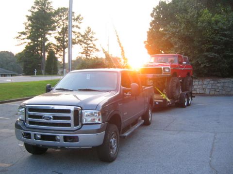 2005 Ford F-250 - A gray 2005 Ford F-250 is seen from the front, towing a red Ford Bronco on a trailer during sunset.