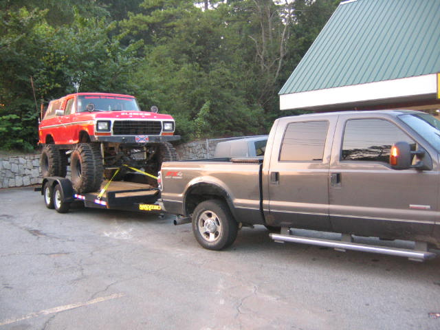 Red lifted Ford Bronco on trailer towed by gray Ford F-250 pickup truck
