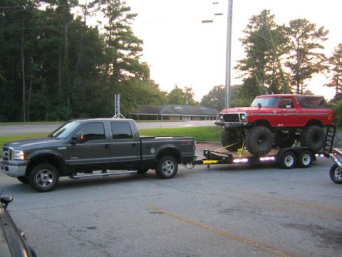 2005 Ford F-250 - A gray 2005 Ford F-250 Super Duty pickup truck tows a red lifted Ford Bronco on a trailer.