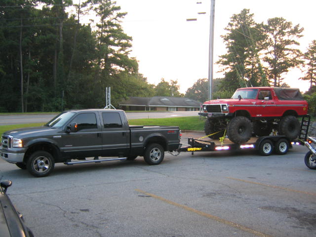 Gray 2005 Ford F-250 Super Duty pickup truck towing a red lifted Ford Bronco on a trailer