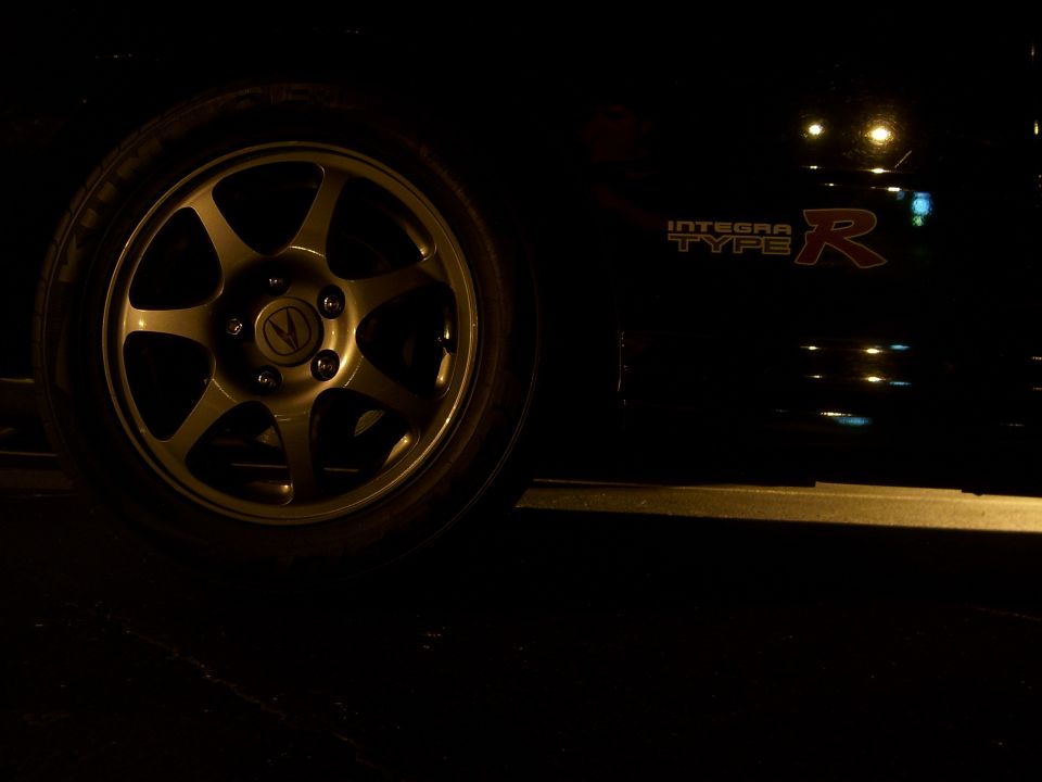 Close-up of a gold five-spoke wheel and the side panel of a black car with an 'INTEGRA TYPE R' badge