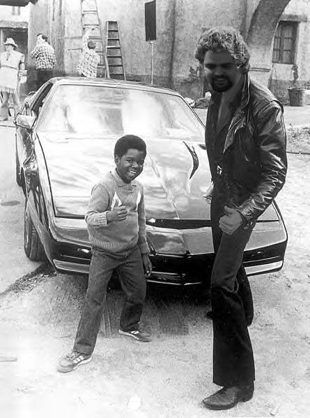 1985 Ford Bronco - A boy and a man pose in front of a black sports car, possibly during a film shoot.