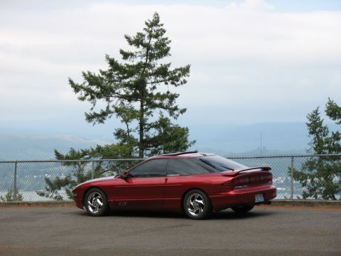 1997 Ford Probe - A red 1997 Ford Probe GT is parked overlooking a valley with trees and a fence in the foreground.