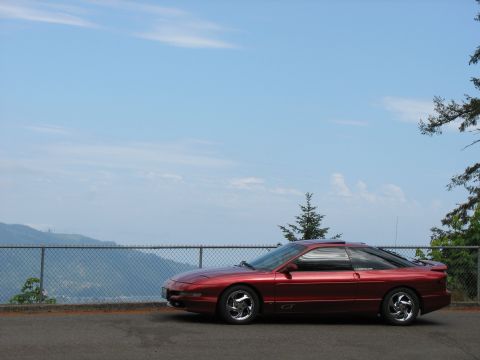 1997 Ford Probe - A red 1997 Ford Probe GT is parked on the side of the road, overlooking a mountain range under a clear blue sky.