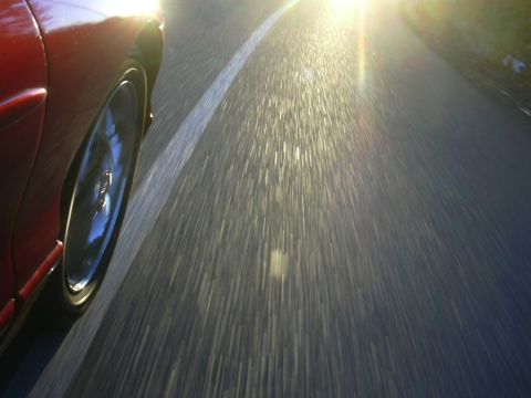 1997 Ford Probe - Sunlight streams across the road as a red car drives forward, blurring the scenery.