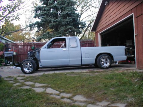 1998 Ford Taurus - A light blue pickup truck is parked outside a garage, missing its front end and appearing to be a project vehicle.
