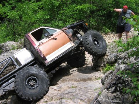 1981 Ford Bronco - A man watches as an off-road vehicle attempts to climb over large rocks on a trail.
