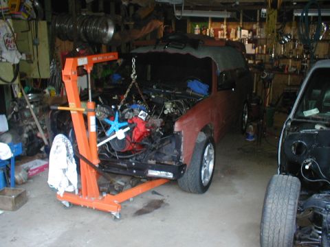 1998 Ford Taurus - An engine hoist is positioned over a car with its engine out, in a cluttered garage setting.