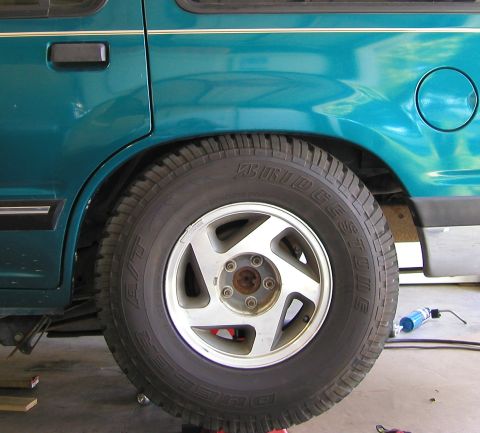 1984 Ford Bronco - Close-up view of the rear wheel and fender of a teal SUV, showing the tire and fuel cap.