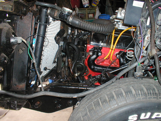 Engine bay with red engine block, black exhaust manifolds, and a radiator. A tire is visible in the foreground