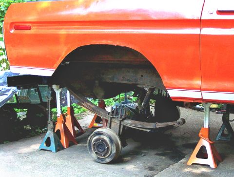 1978 Ford Bronco - The rear suspension of an orange 1978 Ford Bronco is visible while it is raised on jack stands.