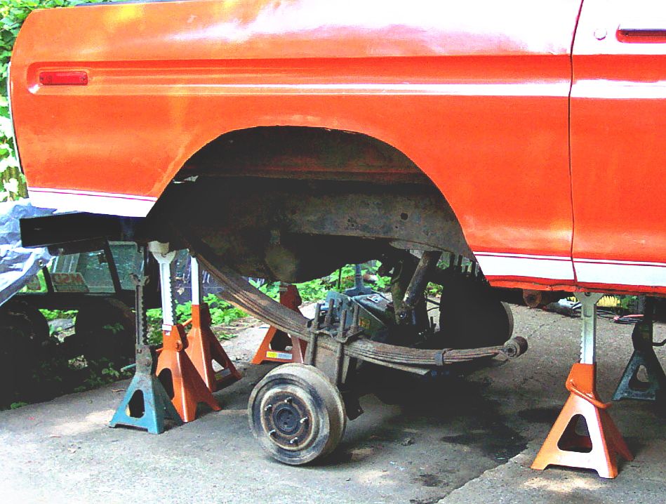 Orange 1978 Ford Bronco rear quarter panel on jack stands, showing leaf spring suspension and part of a wheel