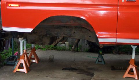 1978 Ford Bronco - The underside of an orange pickup truck is visible as it's supported by jack stands for maintenance.
