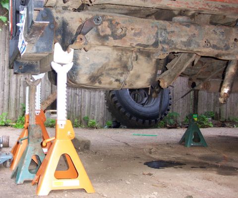 1978 Ford Bronco - The vehicle's undercarriage is visible, supported by multiple jack stands, with a rusty frame and fuel tank.