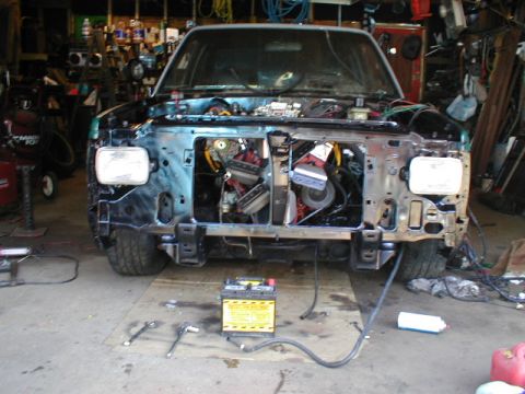 1998 Ford Taurus - The front end of a truck is shown with its hood open, revealing the engine compartment. Tools and a battery are on the floor in front of th…