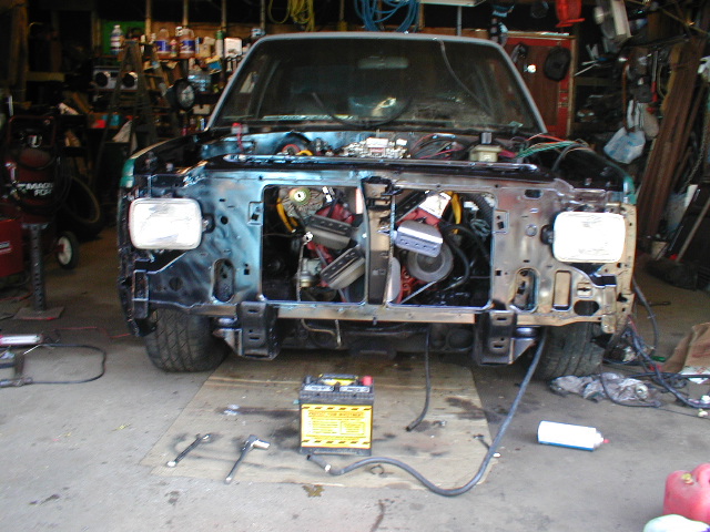 Front end of a truck with engine exposed, battery and tools on the floor