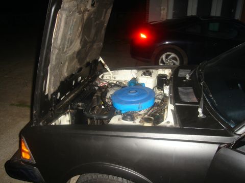 1997 Ford Probe - The engine compartment of a car is shown with the hood raised, while another vehicle is parked behind it.