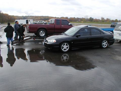 1998 Ford Taurus - A black 1998 Ford Taurus is parked on a wet surface next to a red pickup truck.