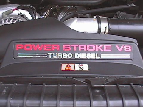 2005 Ford F-250 - Close-up of a black engine cover displaying "POWER STROKE V8 TURBO DIESEL" in red and silver lettering.