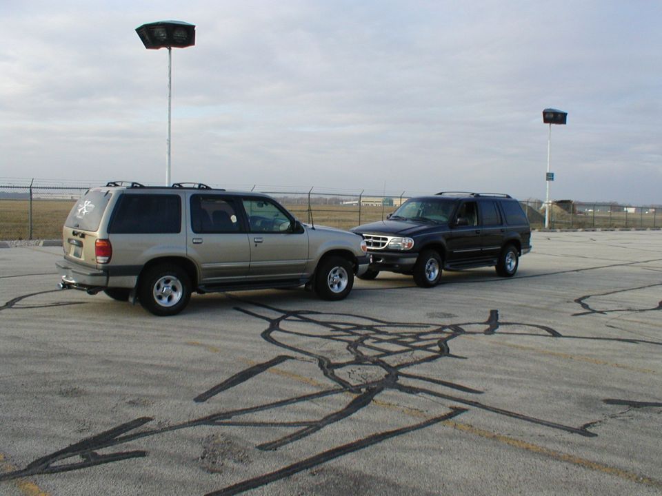 Two Ford Explorer SUVs, one tan and one dark, parked nose-to-nose on an empty lot with skid marks