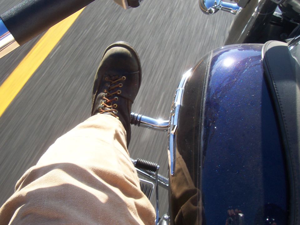 Rider's perspective from a motorcycle, showing boot and blue bodywork