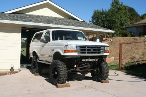 1992 Ford Bronco - A white 1992 Ford Bronco SUV is shown with a lifted suspension and oversized tires in front of a residential garage.