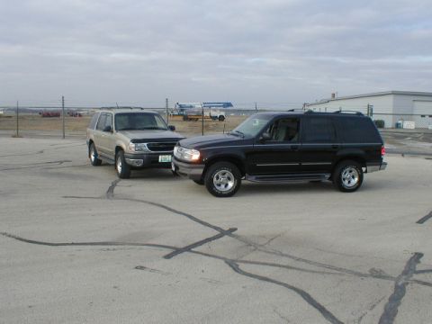 1998 Ford Taurus - Two SUVs are parked on a paved lot under an overcast sky.