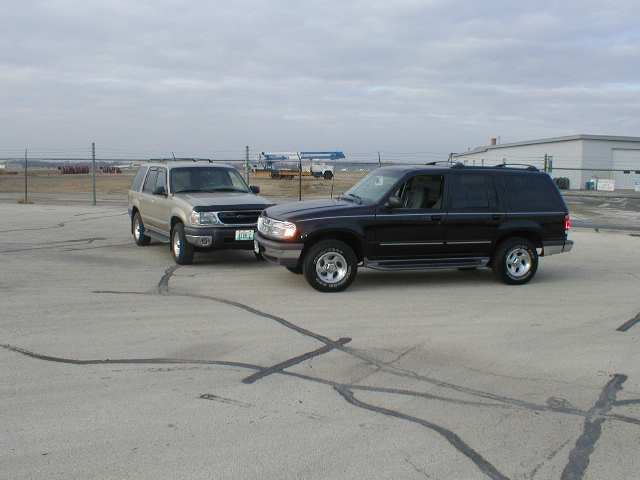 black SUV parked next to tan SUV, both facing right, cloudy sky