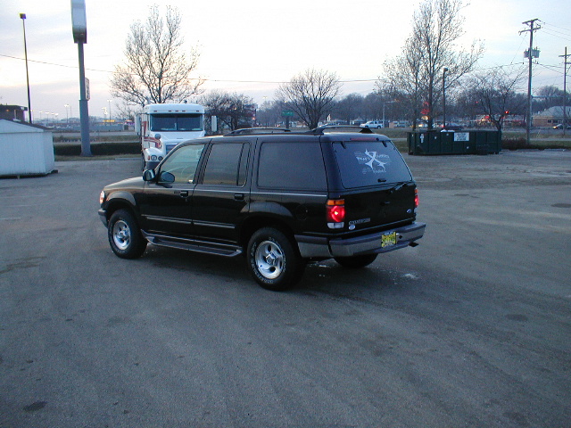 Black Ford Explorer SUV viewed from rear three-quarter on pavement with semi truck in background
