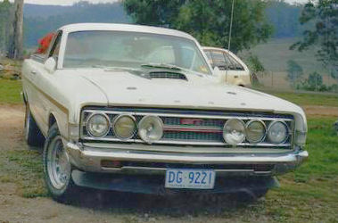 2002 Ford Crown Victoria - A white 1970 Ford Falcon XY GTHO Phase III is parked outdoors, with another vehicle visible behind it.
