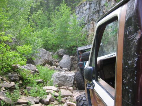 1981 Ford Bronco - Two vehicles on a challenging rocky trail in a wooded, mountainous area.