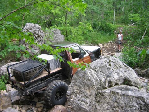 1981 Ford Bronco - A person watches as a heavily modified pickup truck maneuvers through a challenging, rocky off-road course.