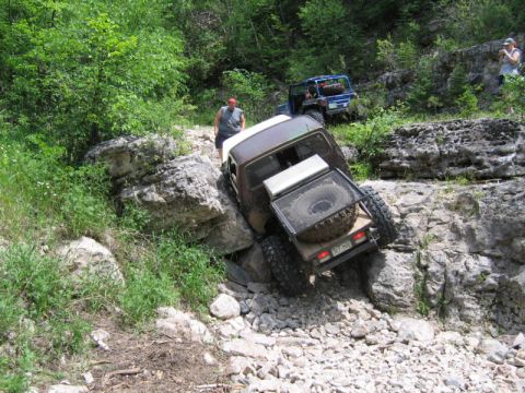 1981 Ford Bronco - Off-road vehicles tackle a challenging rocky path with dense foliage on the sides.