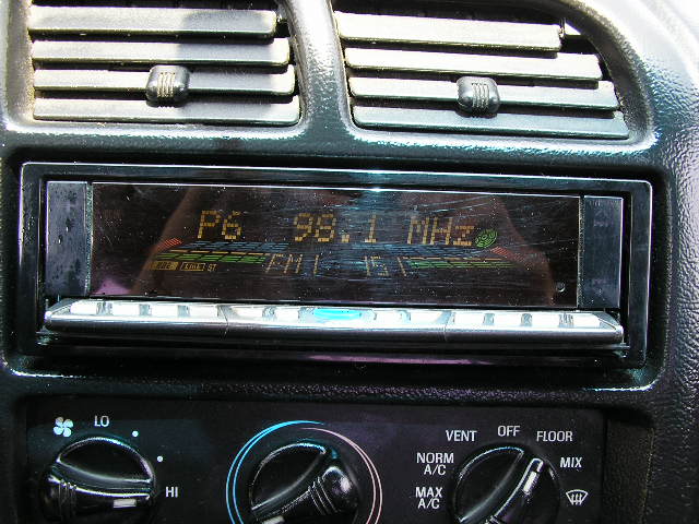 Car interior showing an aftermarket radio display and climate control knobs. Radio shows 'P6 98.1 MHZ'